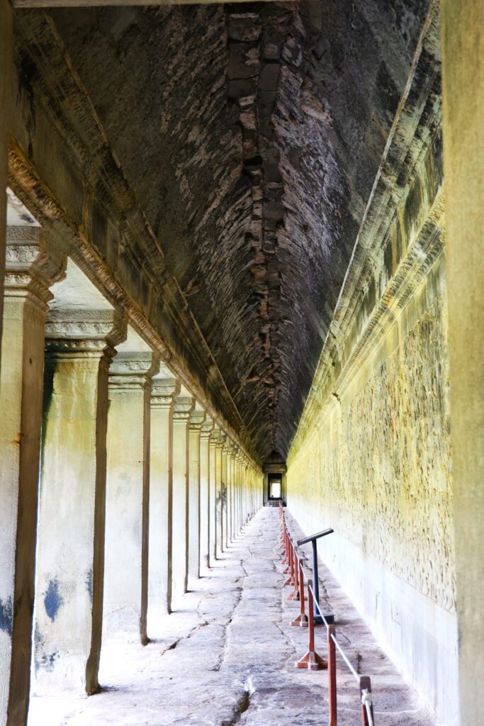 Długi, kamienny korytarz świątyni Angkor z rzeźbionymi reliefami na ścianach.